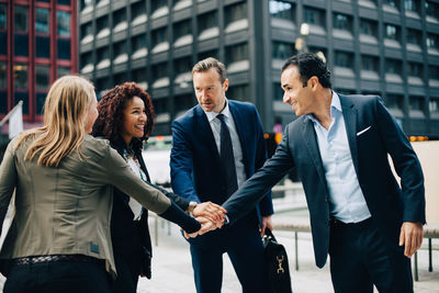 Smiling multi-ethnic business people stacking hands against building in city