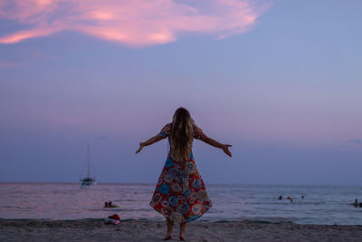 Rear view of woman on beach against sky during sunset