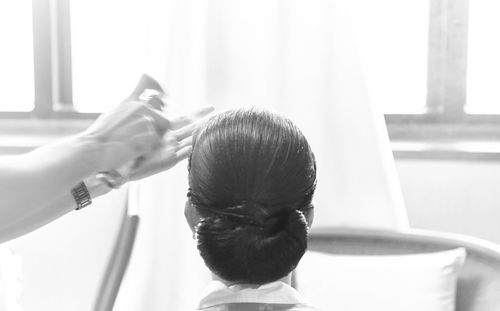 Cropped image of stylist spraying from can on woman head at salon