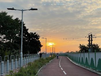 Street amidst trees against sky during sunset