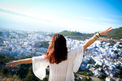 Rear view of woman looking at cityscape against sky