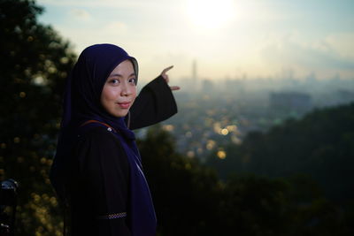 Optical illusion of beautiful young woman holding building while standing against sky