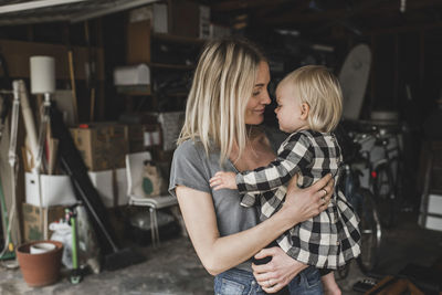 Loving mid adult mother carrying daughter at storage room