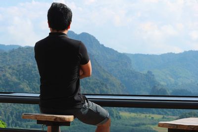 Rear view of man sitting on seat against mountains