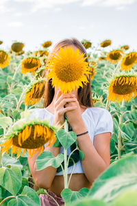 The girl covers her face with a sunflower in a field in the sun. freedom and local tourism