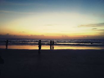 Silhouette people on beach against sky during sunset