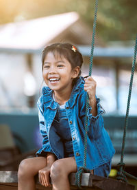 Cheerful girl sitting on swing at playground