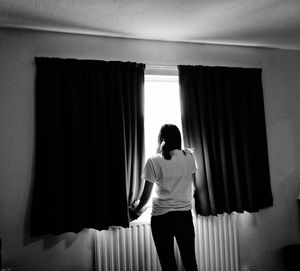 Rear view of woman looking through window at home