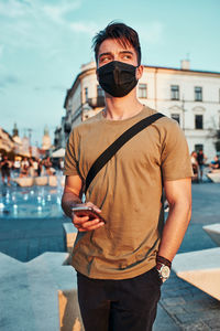 Young man wearing mask looking away while standing outdoors