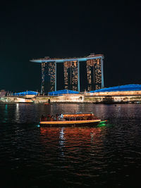 Illuminated city by river against sky at night
