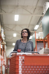 Customer looking away while holding shopping cart in hardware store