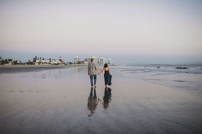 Mid-40's couple holding hands and walking barefoot along the beach