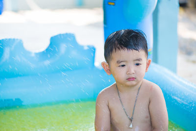 Cute shirtless boy in sprinkler at playground