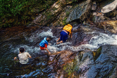 High angle view of children playing in river flowing over rock formations at forest