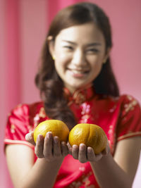 Portrait of smiling woman with oranges standing against backdrop