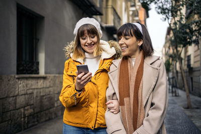 Happy young woman standing on mobile phone in city