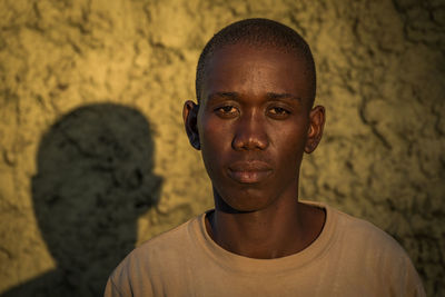 Portrait of serious young man standing against wall on sunny day