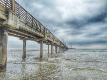 Bridge over sea against cloudy sky