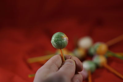 Cropped hand holding colorful lollipop over red fabric