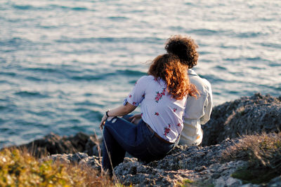 Woman sitting on rock looking at sea