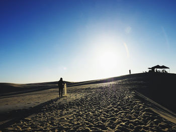 Silhouette man standing on sand against clear sky