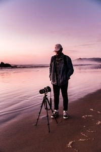 Full length of man photographing sea against sky during sunset