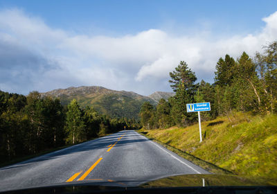 Road sign by trees against sky