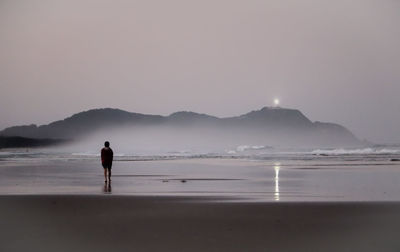 Rear view of man walking on sand against sea during sunset