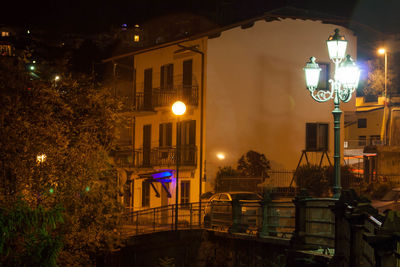 Illuminated street light in city against sky at night