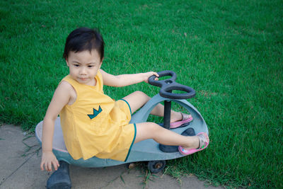 Cute  asian girl, little preschooler child sitting on plastic toy car wearing yellow casual dress.