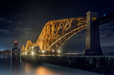 Illuminated bridge over river against sky at night