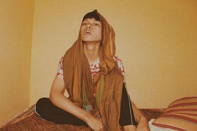 Portrait of young woman sitting against wall at home