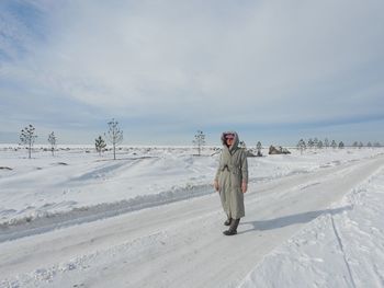 Rear view of woman walking on snow covered field against sky