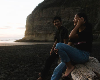 Young woman sitting on rock at beach against sky