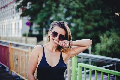 Young woman wearing sunglasses standing by railing