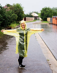 Portrait of woman wearing raincoat standing on road in rainy season