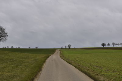 Empty road amidst field against sky