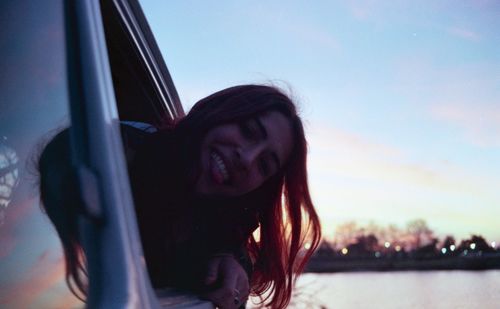 Portrait of smiling young woman in car against sky
