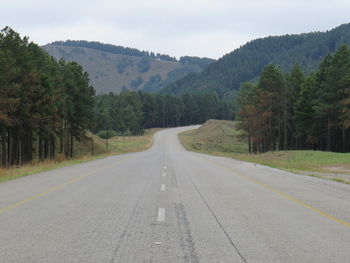 Road amidst trees and mountains against sky