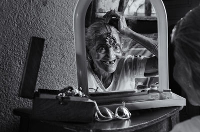 Reflection of cheerful senior woman wearing jewelry on mirror at home