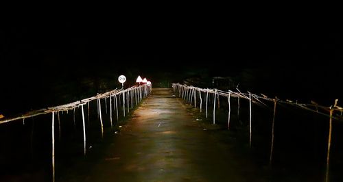 Illuminated road leading towards bridge against sky at night