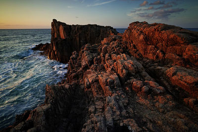 Rock formation on sea against sky during sunset