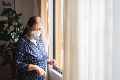 Young woman looking through window at home