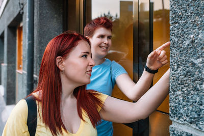 Man and woman pointing by wall