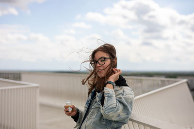 Young woman drinking drink with umbrella standing against sky