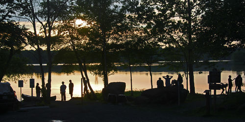 Silhouette people standing by trees against sky during sunset