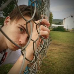 Close-up portrait of young man leaning on chainlink fence
