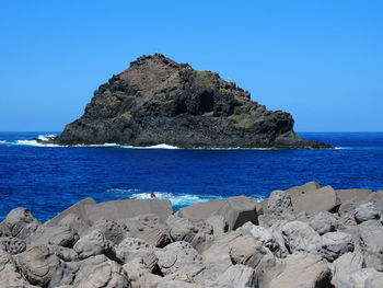 Rock formations by sea against clear blue sky