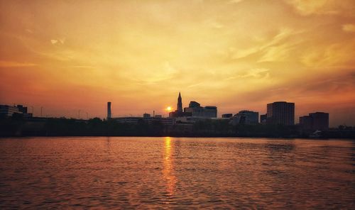 Scenic view of river by buildings against sky during sunset