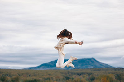 Side view of woman with arms raised standing on mountain against sky